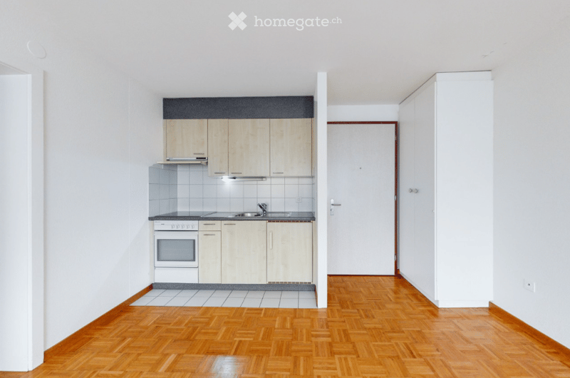 Empty kitchen and adjacent room with light wood cabinets, stainless steel appliances, and wooden flooring.