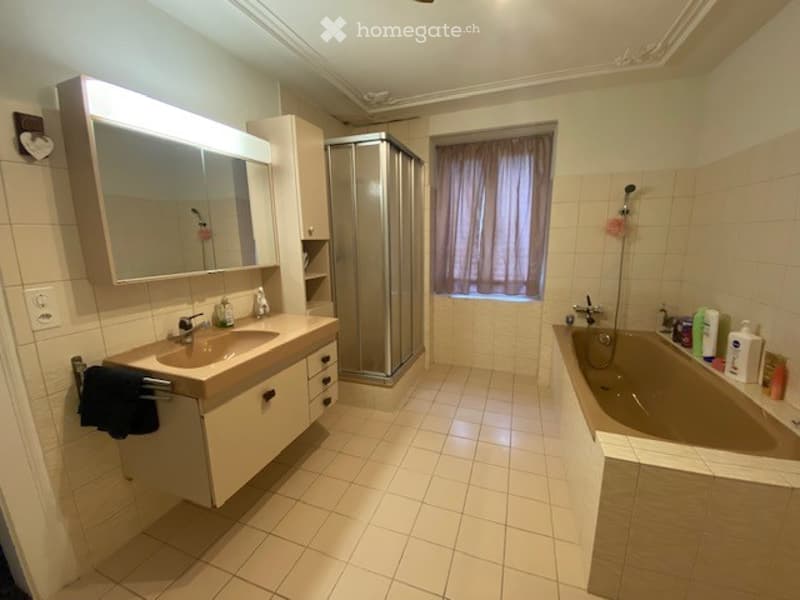 Modern bathroom with a large mirror, sink, bathtub, and shower. The space features tiled walls and floor, with a window covered by a curtain.