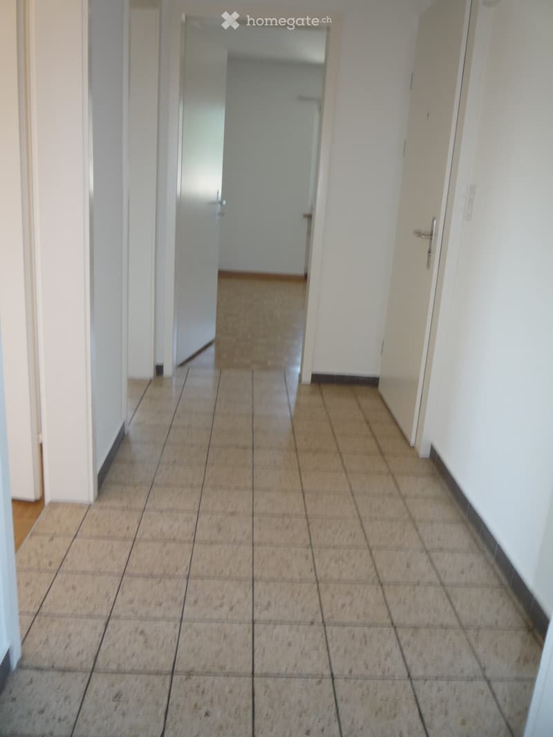 Empty hallway with tiled floor and white walls, featuring a closed door at the end.