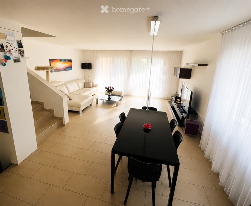 Bright, open living and dining area with white walls, tiled floor, large windows with white curtains, a cream-colored sofa, a glass coffee table, a black dining table with chairs, a cat tree, a television, and a floor lamp.