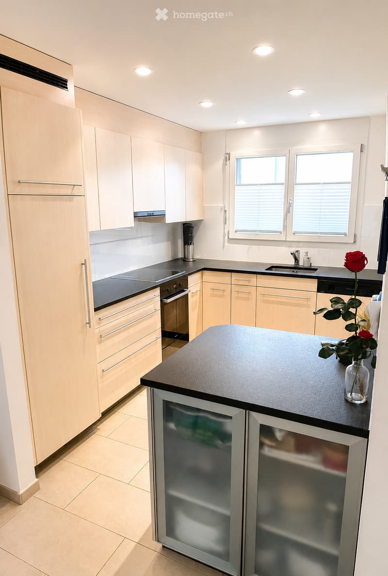 Modern kitchen with light wood cabinets, stainless steel appliances, and a central island with a black countertop.