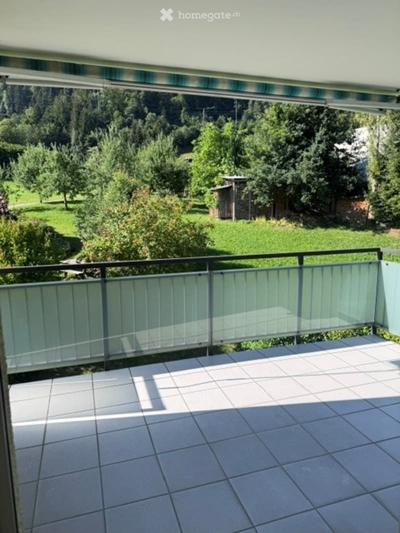 Balcony with tiled floor, glass railing, and scenic view of a green landscape with trees and a small shed.