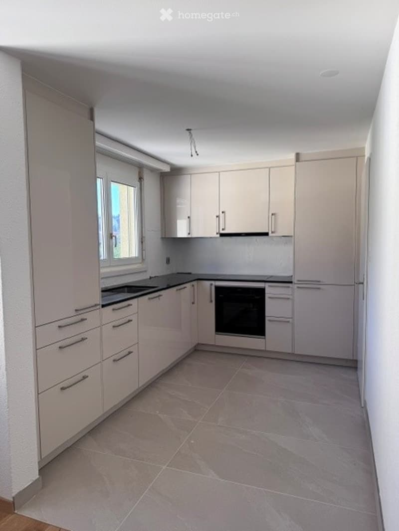 Modern kitchen with light-colored cabinets, stainless steel appliances, and tiled flooring.