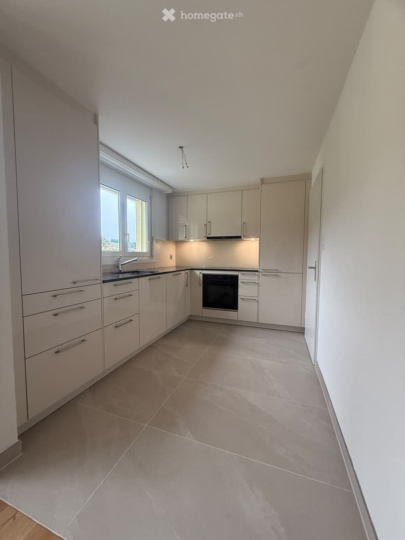 Modern kitchen with light-colored cabinets, a sink, and an oven, featuring tiled flooring and ample natural light from a window.