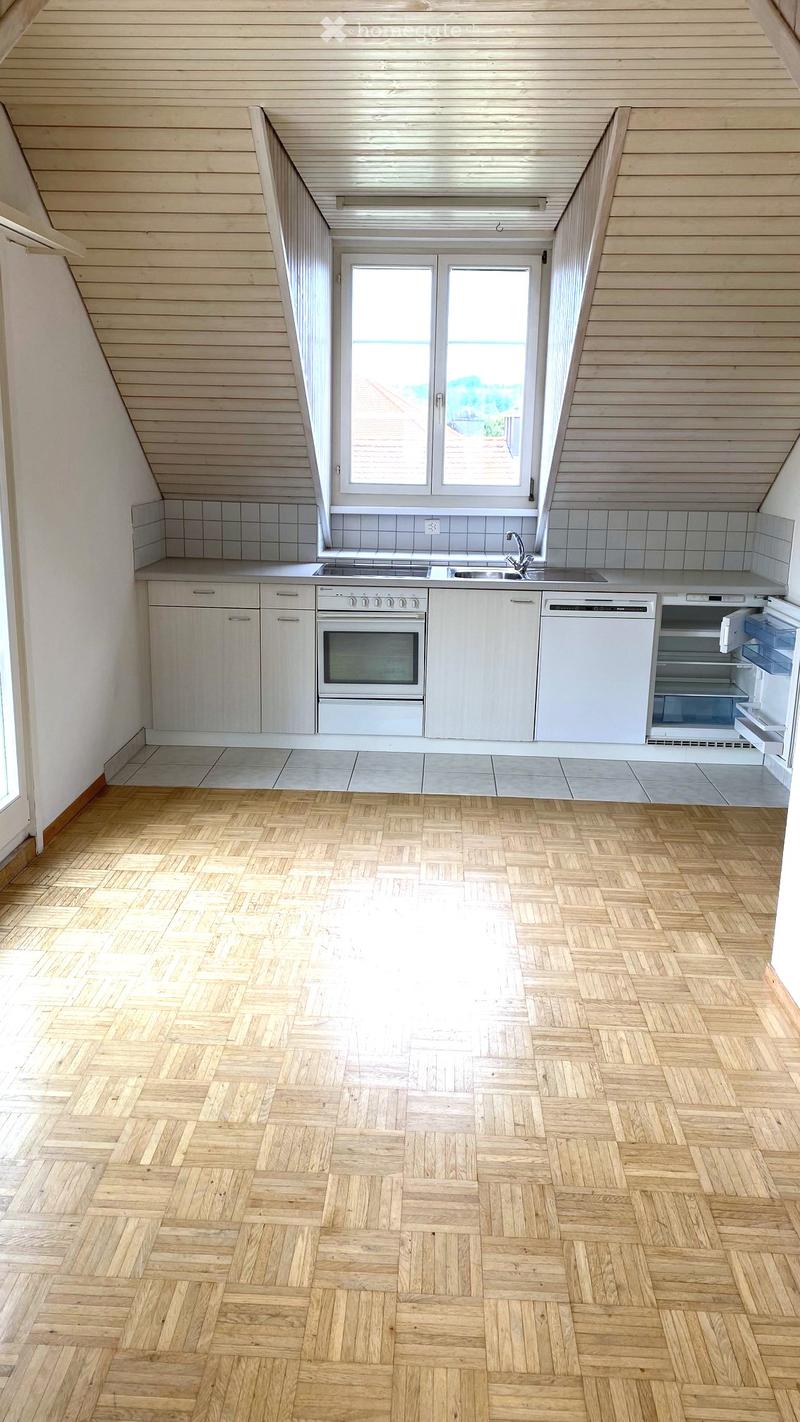 Bright, modern kitchen with white cabinets, wooden herringbone flooring, and built-in appliances including an oven, dishwasher, and refrigerator. Large window provides natural light.