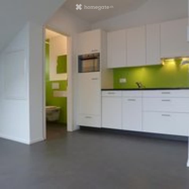 Open-plan kitchen and living area with white cabinets, green accent lighting, and grey flooring. No furniture or equipment present.