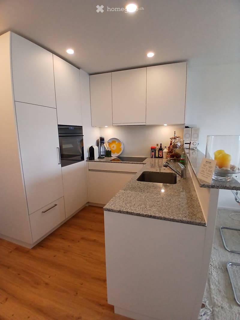 Modern kitchen with white cabinets, granite countertop, sink, and various appliances including an oven and coffee maker.