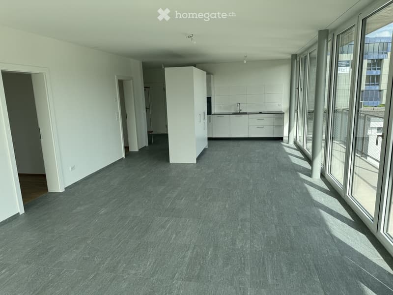 Empty room with grey tiled floor, white walls, and large windows. No furniture or equipment present.