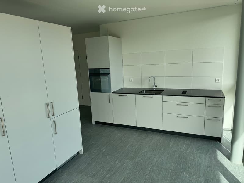 Modern kitchen with white cabinets, a black countertop, a sink, and a faucet. The floor is made of dark grey tiles.