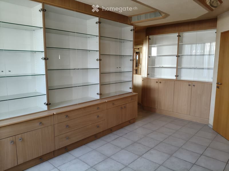Empty room with wooden display cabinets and glass shelves, tiled floor, and wooden door frame.