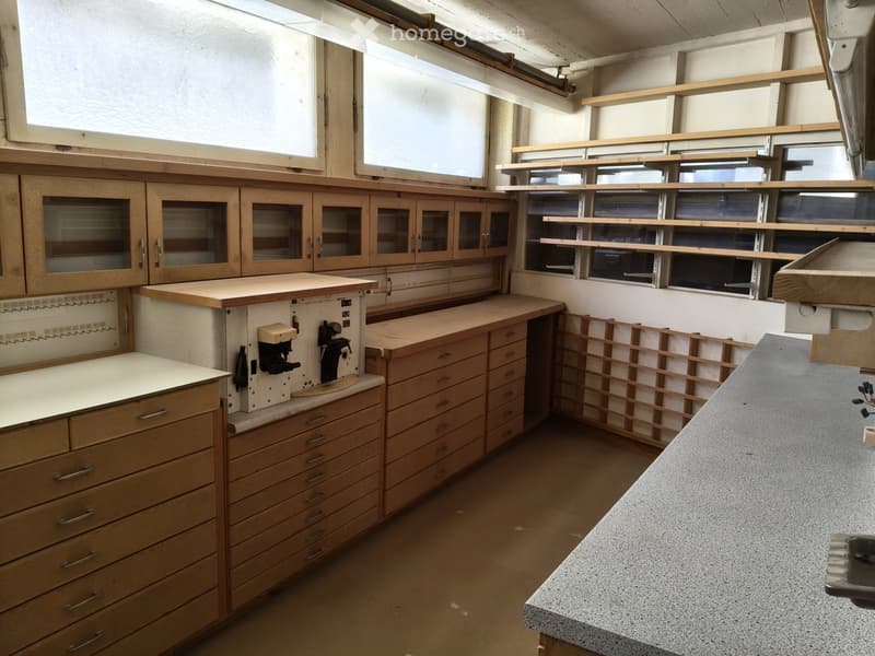 Well-lit workshop with wooden cabinets, drawers, and a countertop, featuring built-in shelves and a large window.