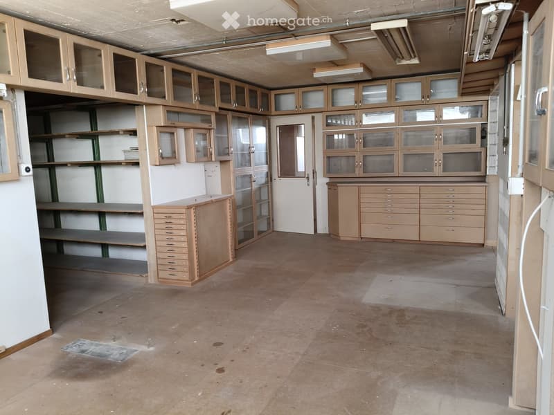 Empty room with wooden cabinets, shelves, and drawers, featuring a concrete floor and exposed ceiling pipes.