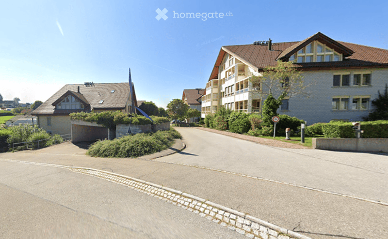 Residential street with multi-story houses, garage, and landscaped greenery.