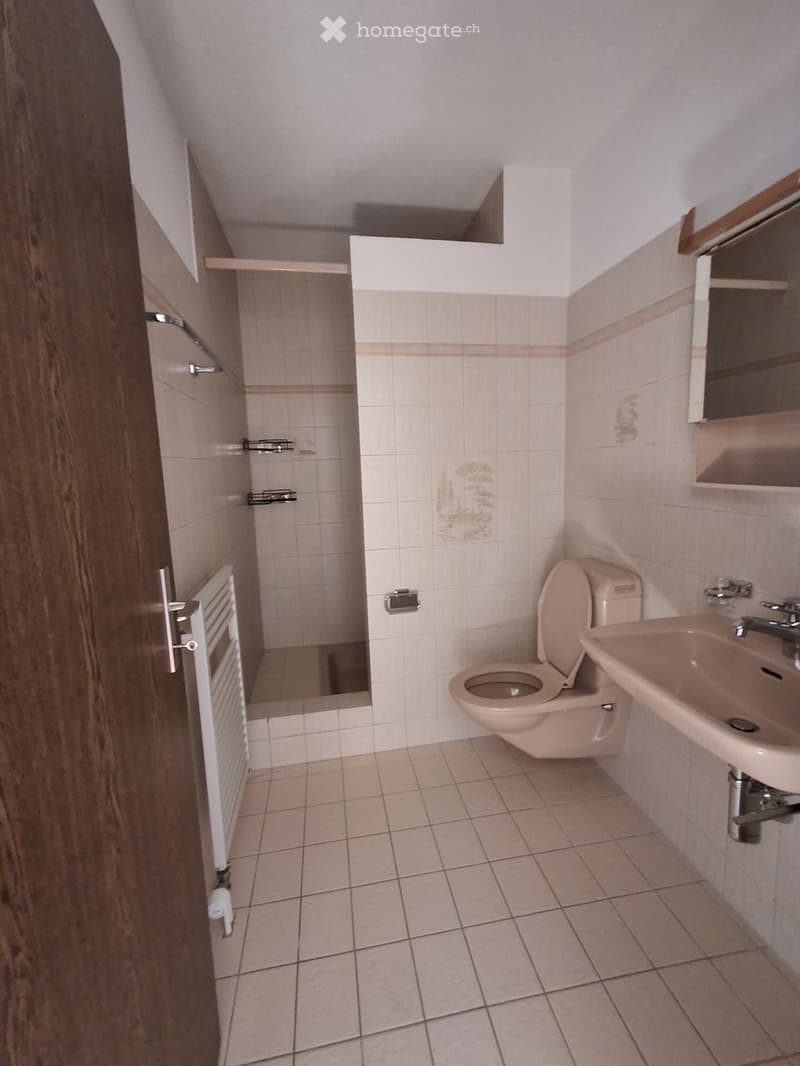 Small bathroom with beige tiles, a toilet, a sink, a mirror, and a shower area with a glass door.