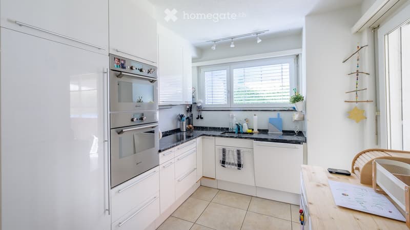 Modern kitchen with white cabinets, stainless steel appliances, granite countertops, and a wooden dining area.