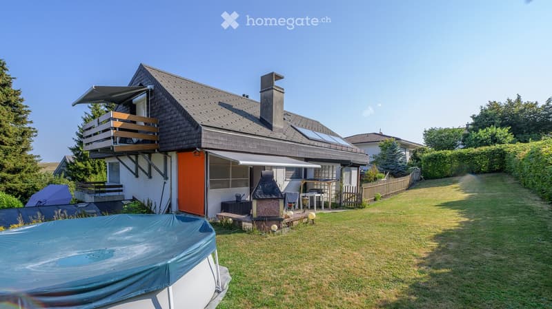 Two-story house with a grey roof, orange front door, balcony, patio, barbecue, and a covered swimming pool in the yard.