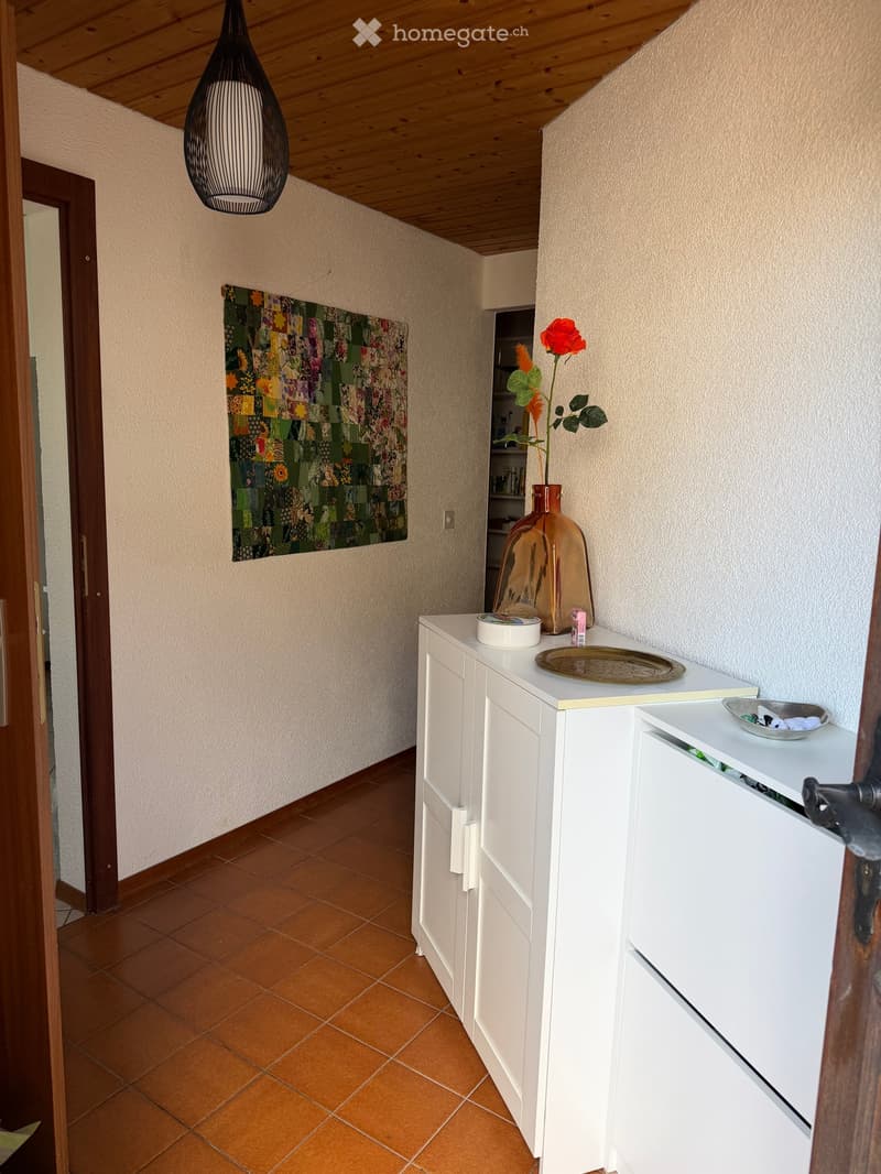 Hallway with tiled floor, white cabinet, vase with flower, and decorative plate on top.