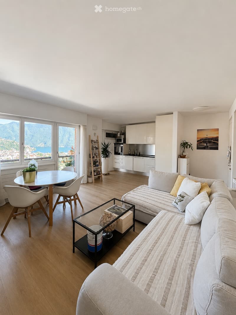 Modern open-plan living and dining area with a sofa, coffee table, dining table, chairs, and a small kitchen area with cabinets and appliances.