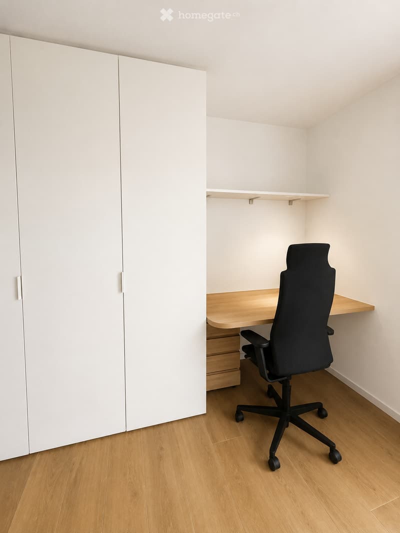 A modern, minimalist room with a wooden floor, white walls, a large white cabinet, a floating desk, a black office chair, and a small shelf.