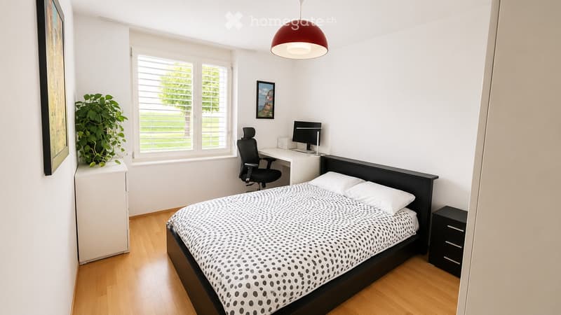 Modern bedroom with a double bed, nightstand, desk with a computer, and a large window with blinds. The room features a wooden floor and white walls.