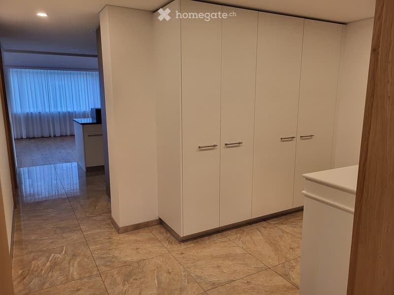 Empty room with white built-in wardrobes, tiled floor, and a view into another room with a desk and window.