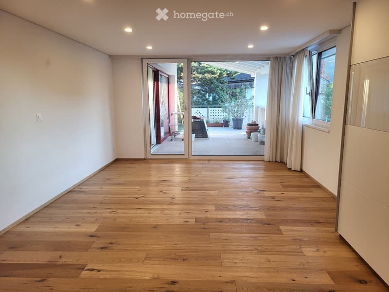 Empty room with wooden flooring, white walls, large windows, and a sliding glass door leading to a patio.