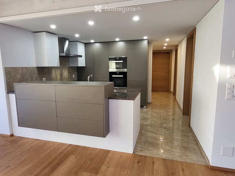 Modern kitchen with grey and white cabinets, a central island, and a built-in oven. The floor is a combination of wooden and tiled surfaces.