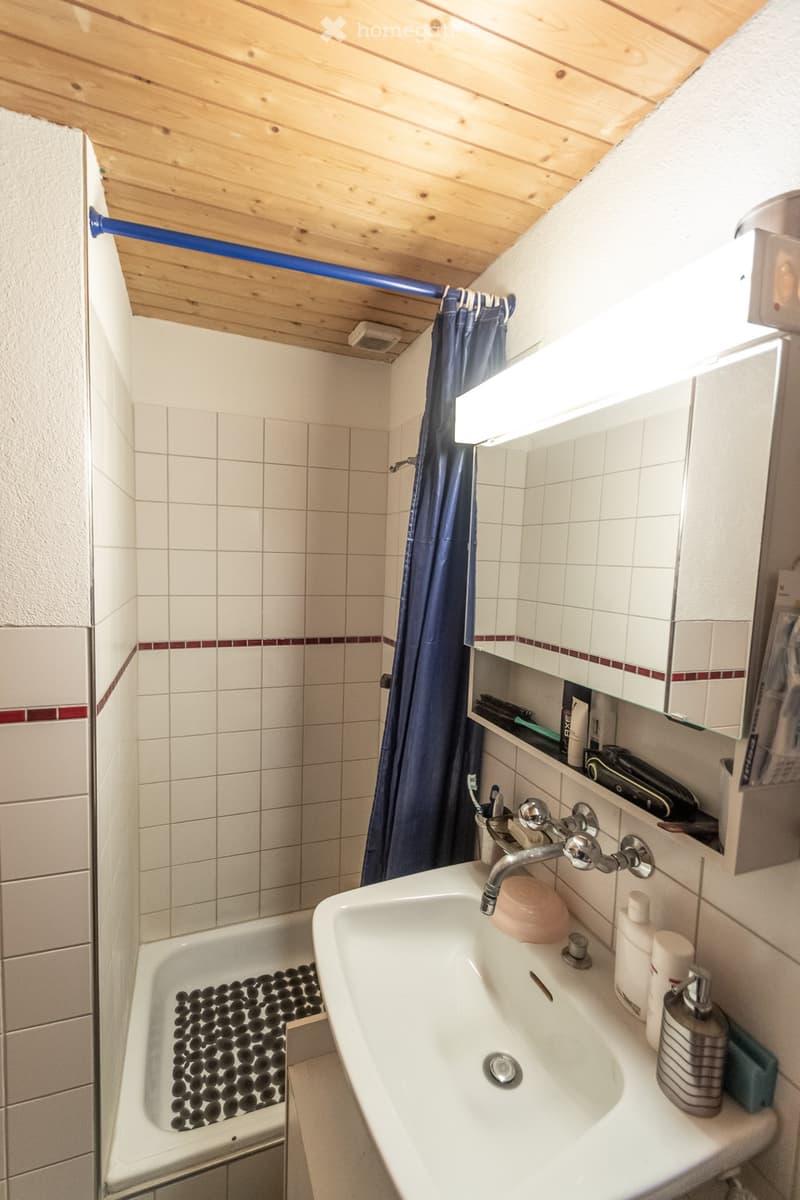 Bathroom with a white sink, bathtub, mirror, and shelves holding toiletries. The bathtub features a black pebble design, and the sink has a chrome faucet.