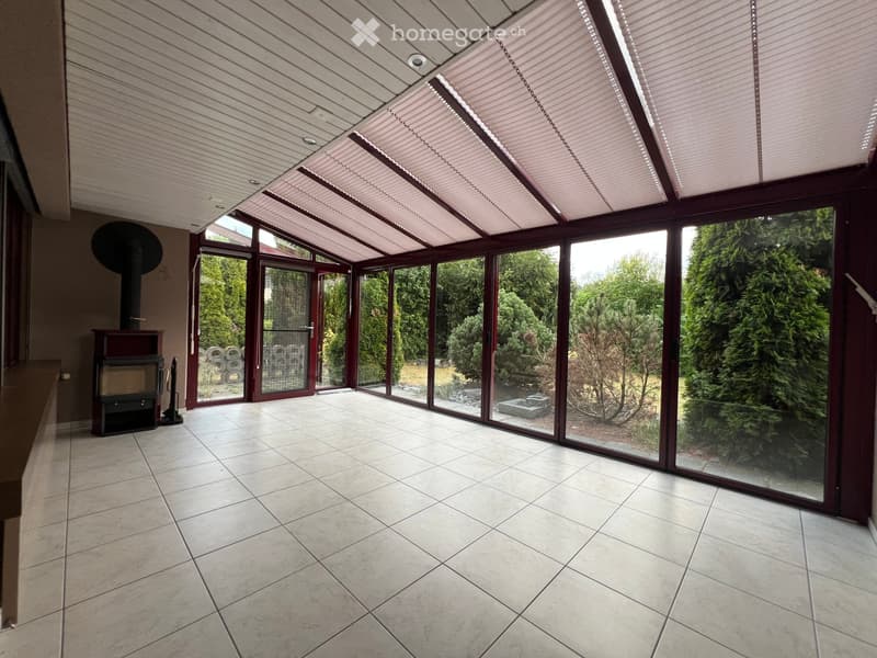 Spacious sunroom with large glass windows and doors, tiled floor, and a fireplace on the left side.