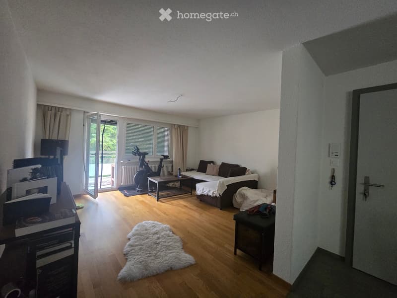 Bright living room with wooden flooring, large windows, a sofa, coffee table, exercise bike, and a white fur rug.