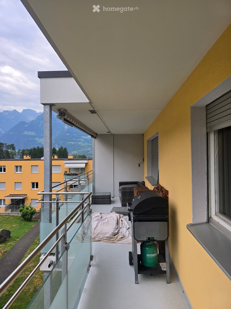 Balcony with a view of mountains, featuring a sofa, a small table, a grill, and a gas cylinder.