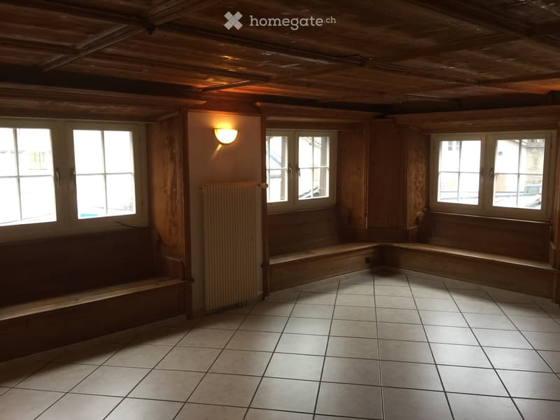Empty room with wooden walls, tiled floor, built-in wooden benches, and large windows letting in natural light.