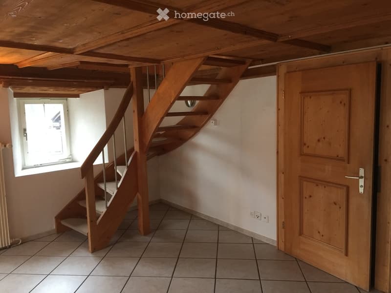 Wooden staircase with metal railing leads to an open wooden door, with a window on the left side providing natural light.