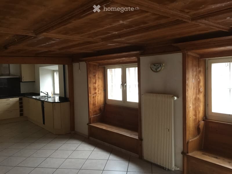 Room with wooden ceiling beams, tiled floor, wooden benches, radiator, sink, and cabinets.
