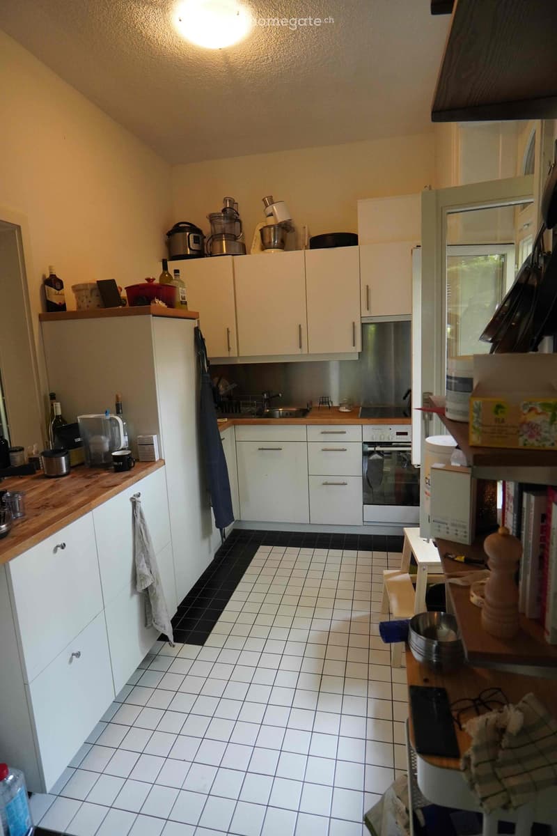 Modern kitchen with white cabinets, stainless steel appliances, and a wooden countertop. Various kitchen items are placed on the counters and shelves.