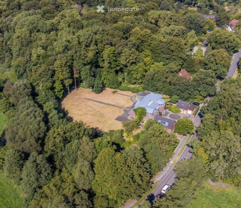 Aerial view of a large, well-maintained garden area with a swimming pool, surrounded by dense greenery and trees.