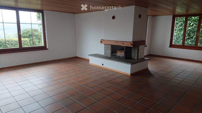 Empty room with tiled floor, white walls, large windows, and a fireplace with a wooden mantel.