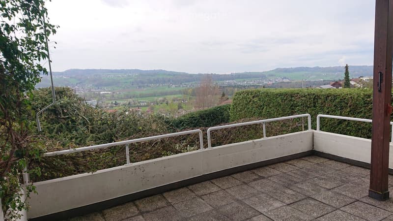 Balcony with tiled floor, white railing, and scenic view of a town and countryside.