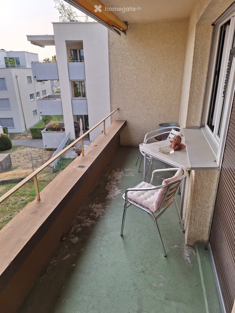 Balcony with green floor, white table, two chairs, and a small stool.
