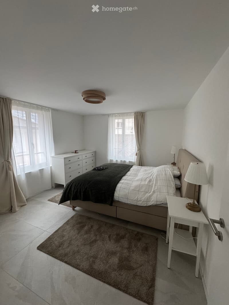 Bedroom with bed, nightstands, lamps, rug, dresser, and windows with curtains