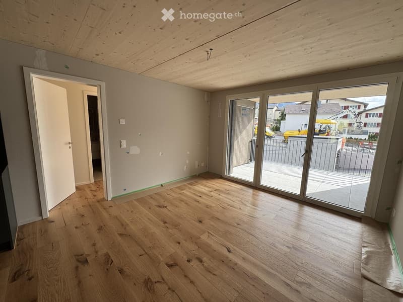 Empty room with wooden flooring, white walls, and large sliding glass doors leading to a balcony.