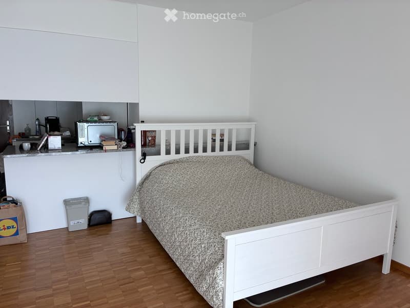 A small bedroom with a single bed, microwave, and a small kitchen area in the corner.