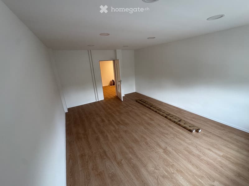 Empty room with light wooden flooring and white walls, featuring a doorway leading to another room.