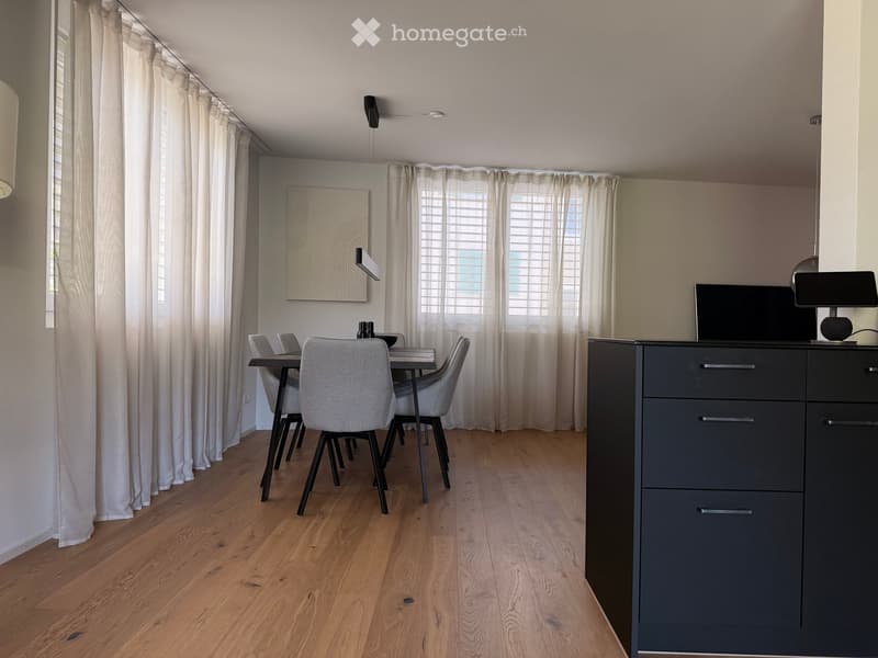 Modern dining area with wooden flooring, grey dining chairs, a black dining table, grey cabinet, and a screen on top.