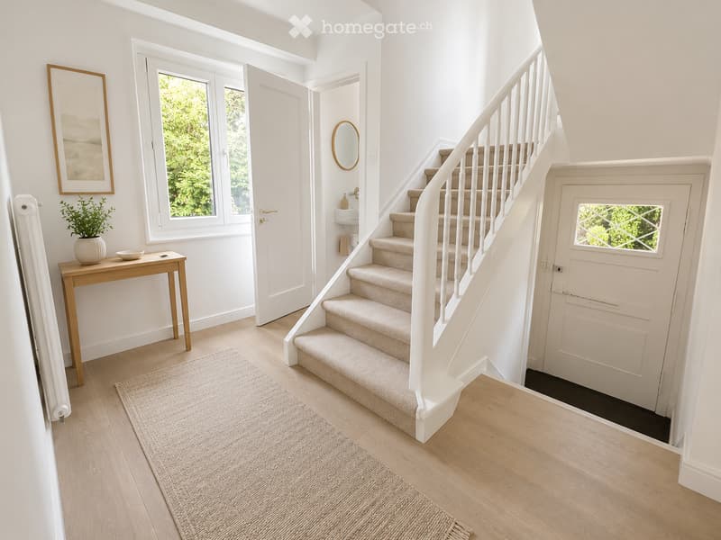 Bright hallway with wooden flooring, a staircase with white railings, a small table with a plant, and a mirror on the wall.
