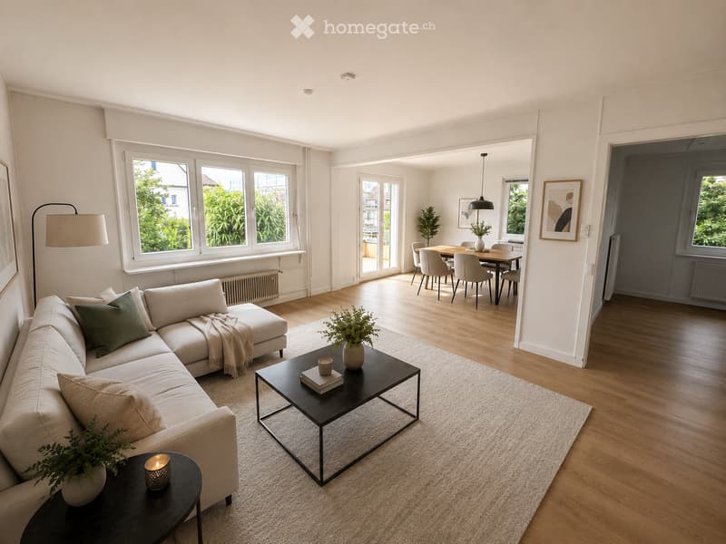 Modern living room with a light-colored sectional sofa, coffee table, side table, and dining area with chairs and a table. Large windows and a view of greenery.