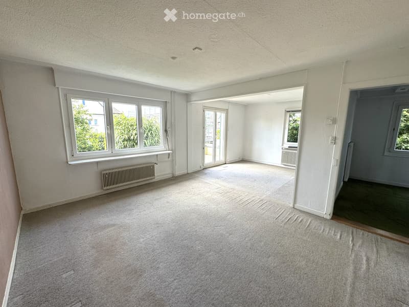 Empty room with white walls, carpeted floor, large windows, and a sliding glass door leading to another space.