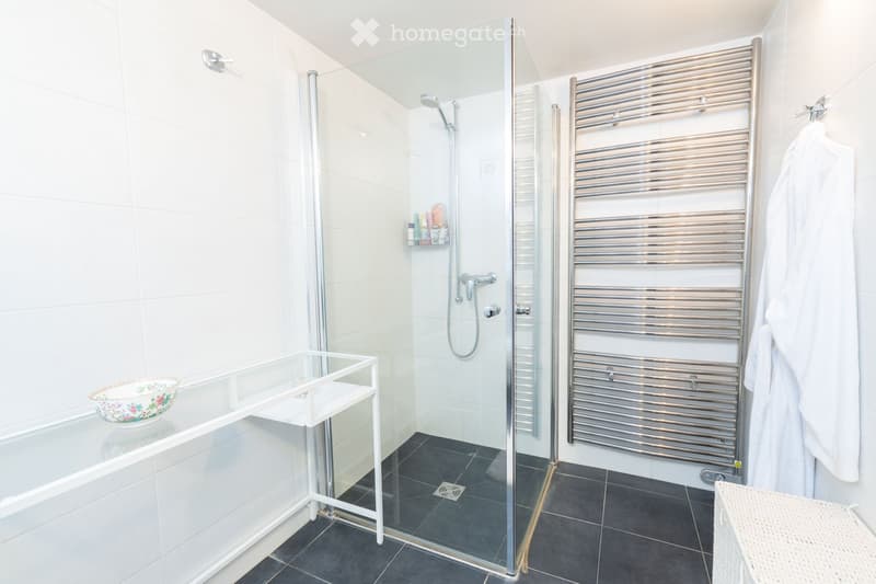 Modern bathroom with a bathtub, glass-enclosed shower, towel rack, and a small table with a decorative bowl.