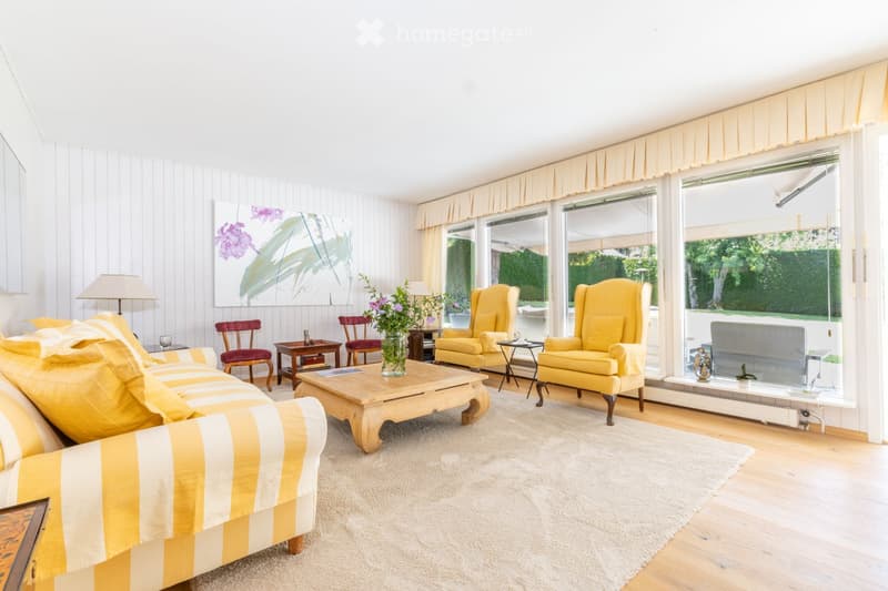 Bright living room with large windows, yellow armchairs, striped sofa, coffee table, side tables, and decorative vases.