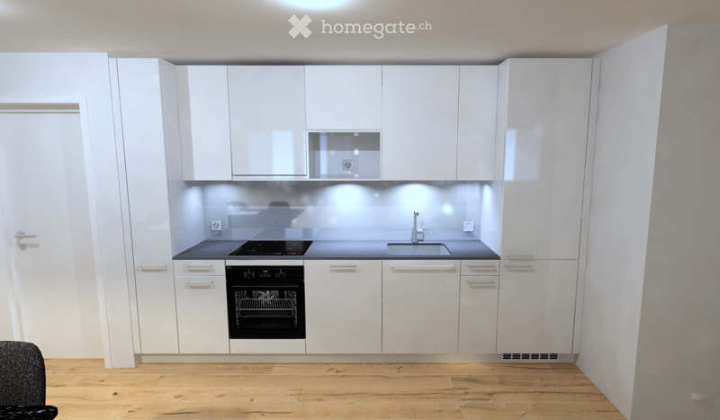 Modern kitchen with white cabinets, black countertops, and built-in appliances including a sink, stove, and oven.